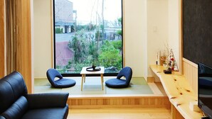 A modern living room with a black leather sofa, a wooden coffee table, and a TV on a wooden stand. - Ocean Aroha Resort (Onna)
