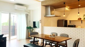 A modern kitchen with a brick backsplash, a wooden dining table, and a sliding glass door leading to a balcony. - Ocean Aroha Resort (Onna)