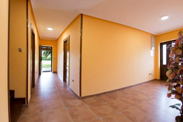 A hallway with yellow walls and tiled flooring, leading to a door with a plant beside it. - Country house Villa Paula (Avilés)