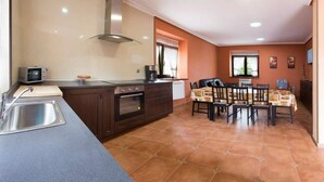 A kitchen with a built-in oven, a microwave, and a sink. There is a dining table with chairs and a window with curtains.