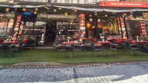 Un edificio con varios balcones, un café y un restaurante en la planta baja, y mesas al aire libre.