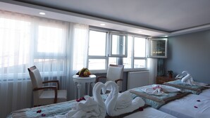 Habitación de hotel con dos camas, una mesita con fruta, una silla y una ventana con cortinas.