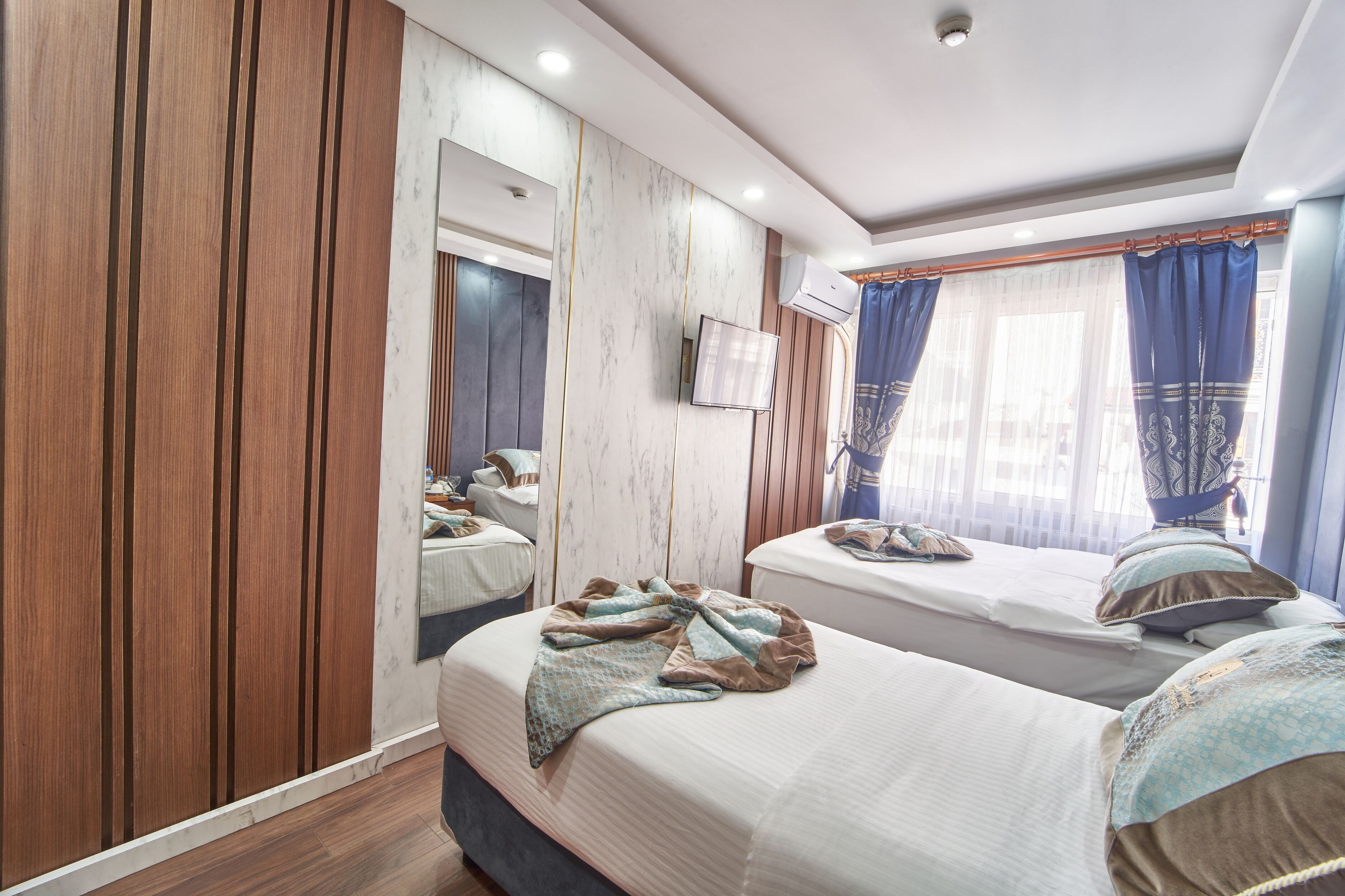 A hotel room with two beds, wooden paneling, a large mirror, and a window with curtains.