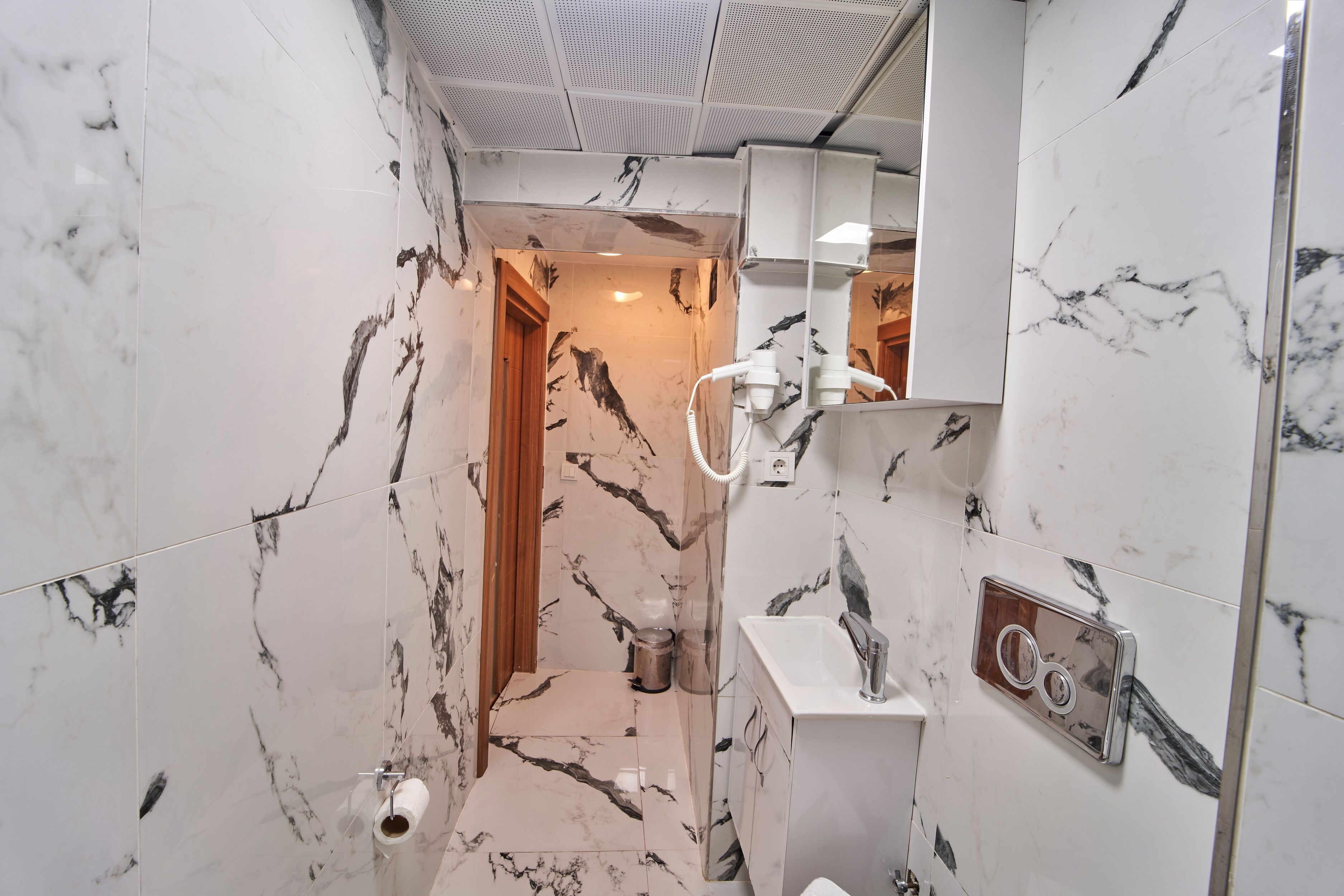 A bathroom with marble walls, a wooden door, a sink, and a shower area.