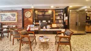 Un área de recepción con un reloj, un letrero que dice Sirkeci Hotel, un mostrador de recepción y un refrigerador.