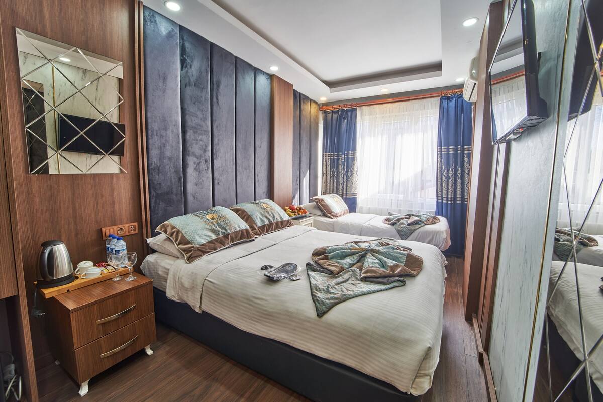 A hotel room with a large bed, a bedside table with a kettle, a mirror, and a wardrobe.