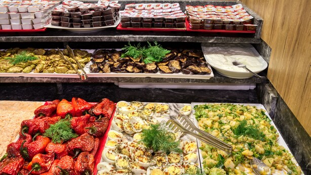 Un bufé con diversos platos, incluyendo pimientos asados, huevos y una variedad de alimentos ya preparados.