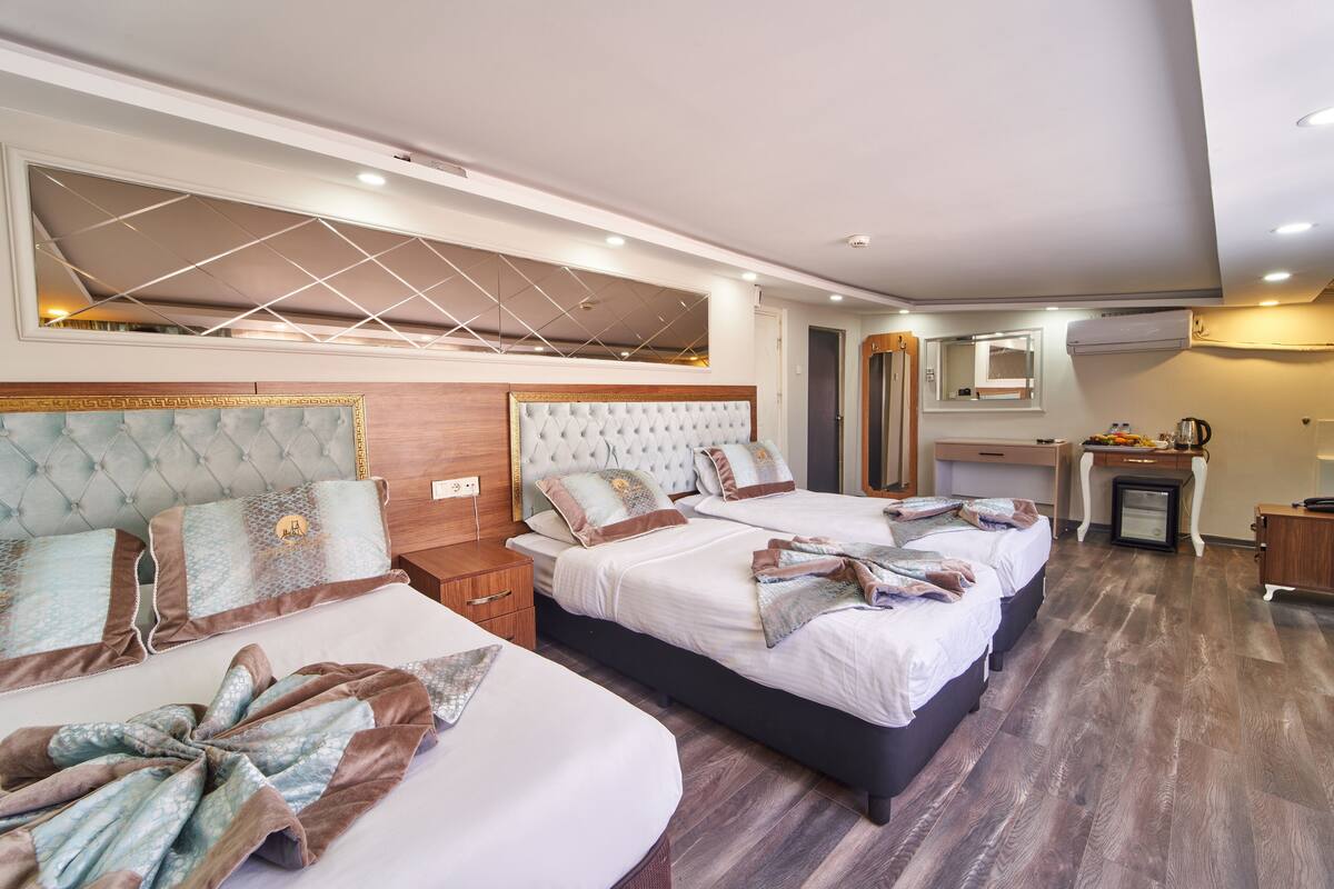 A hotel room with three beds, a desk, and a mirror.