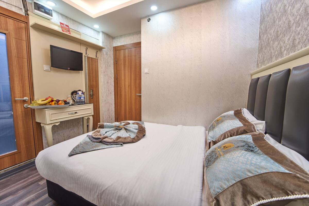 A hotel room with a bed, a TV, a desk with a fruit bowl, and a wardrobe.