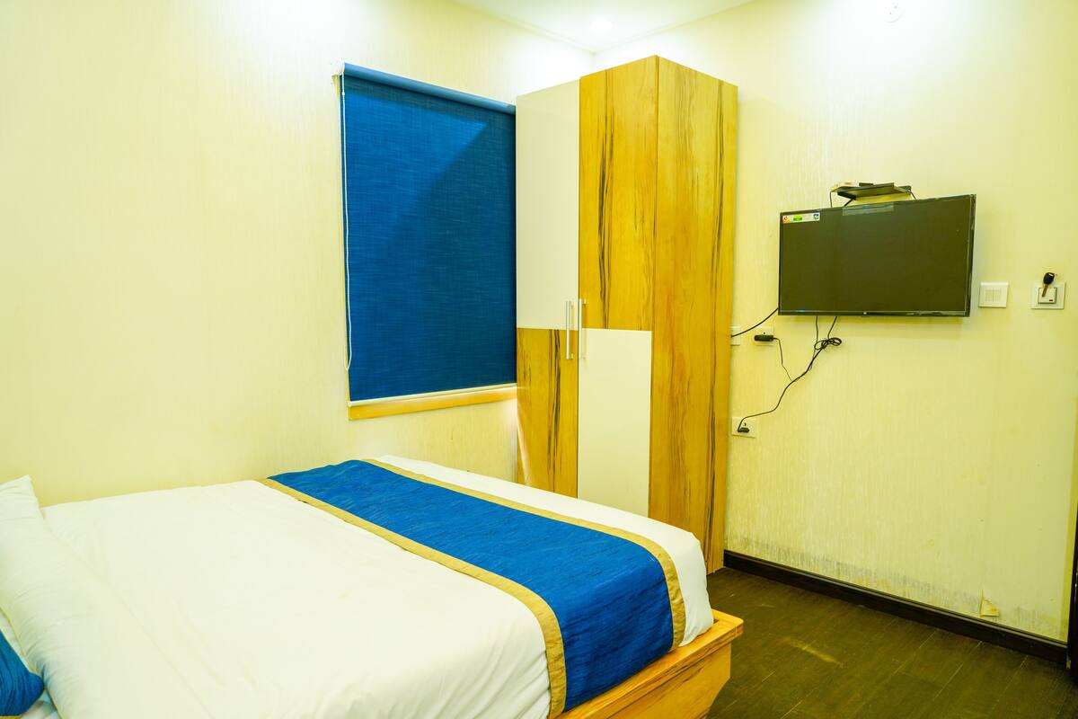 Een hotelkamer met een bed, een kledingkast, een aan de muur bevestigde televisie en een raam met zonwering.
