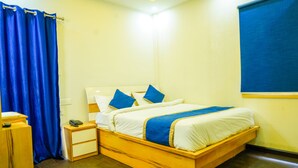 A bedroom with a wooden bed, blue curtains, a bedside table with a phone, and a window with a blind. - Oriental Grand (Ootacamund)