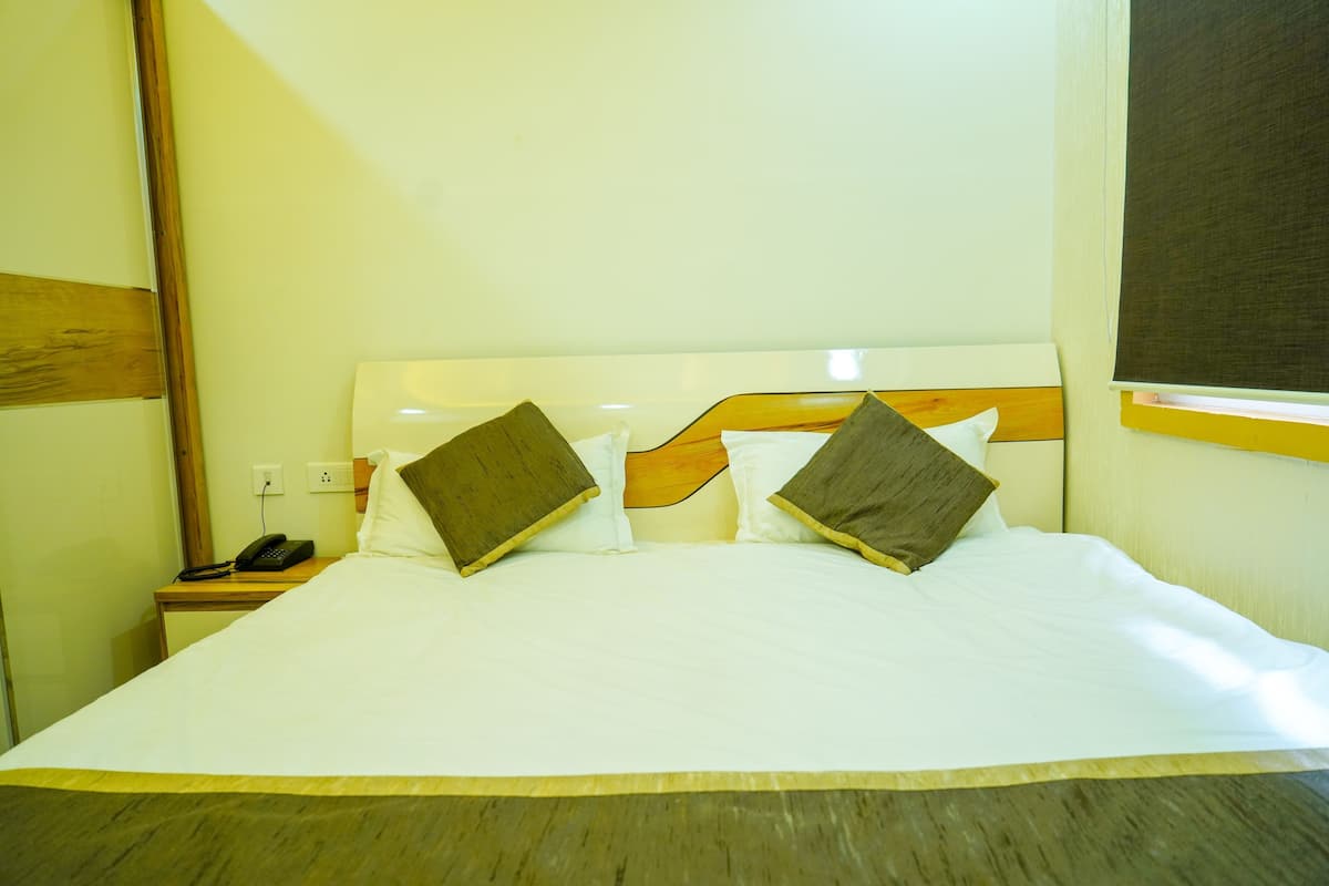 Een hotelkamer met een bed, kussens, een nachtkastje met telefoon en een raam met jaloezieën.
