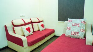 A room with a red and white sofa set, a small table, and a window with a view. - Oriental Grand (Ootacamund)