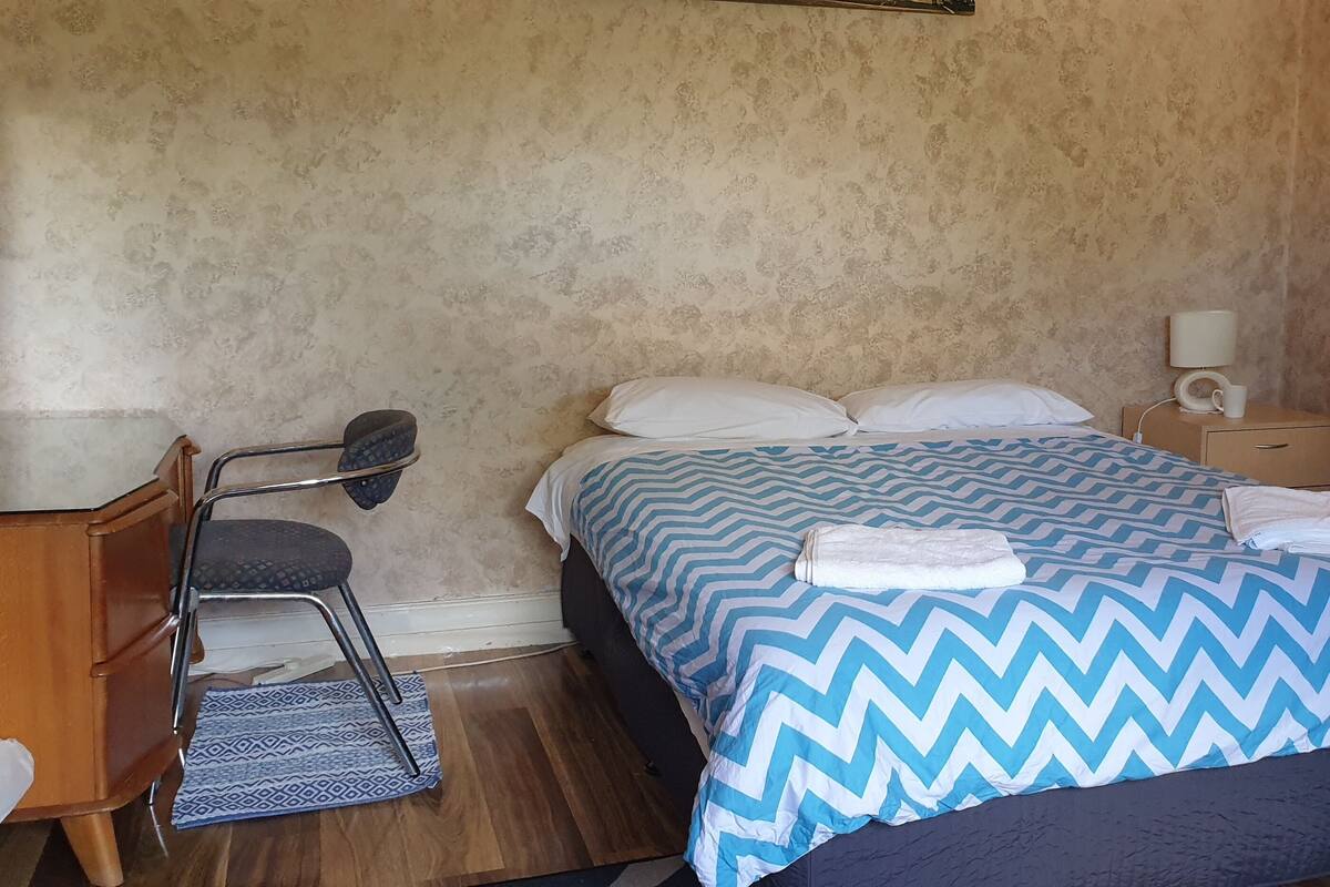 A single bed with a patterned bedspread, a bedside table with a lamp, and a chair.