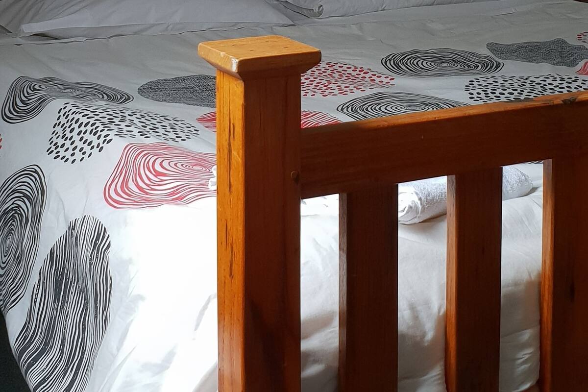 A bed with a wooden headboard, white bedding with abstract patterns, and a framed picture on the wall.