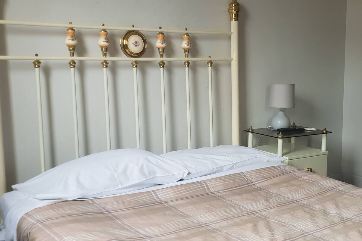 A bed with a plaid bedspread, a white pillow, and a wooden headboard with decorative elements.
