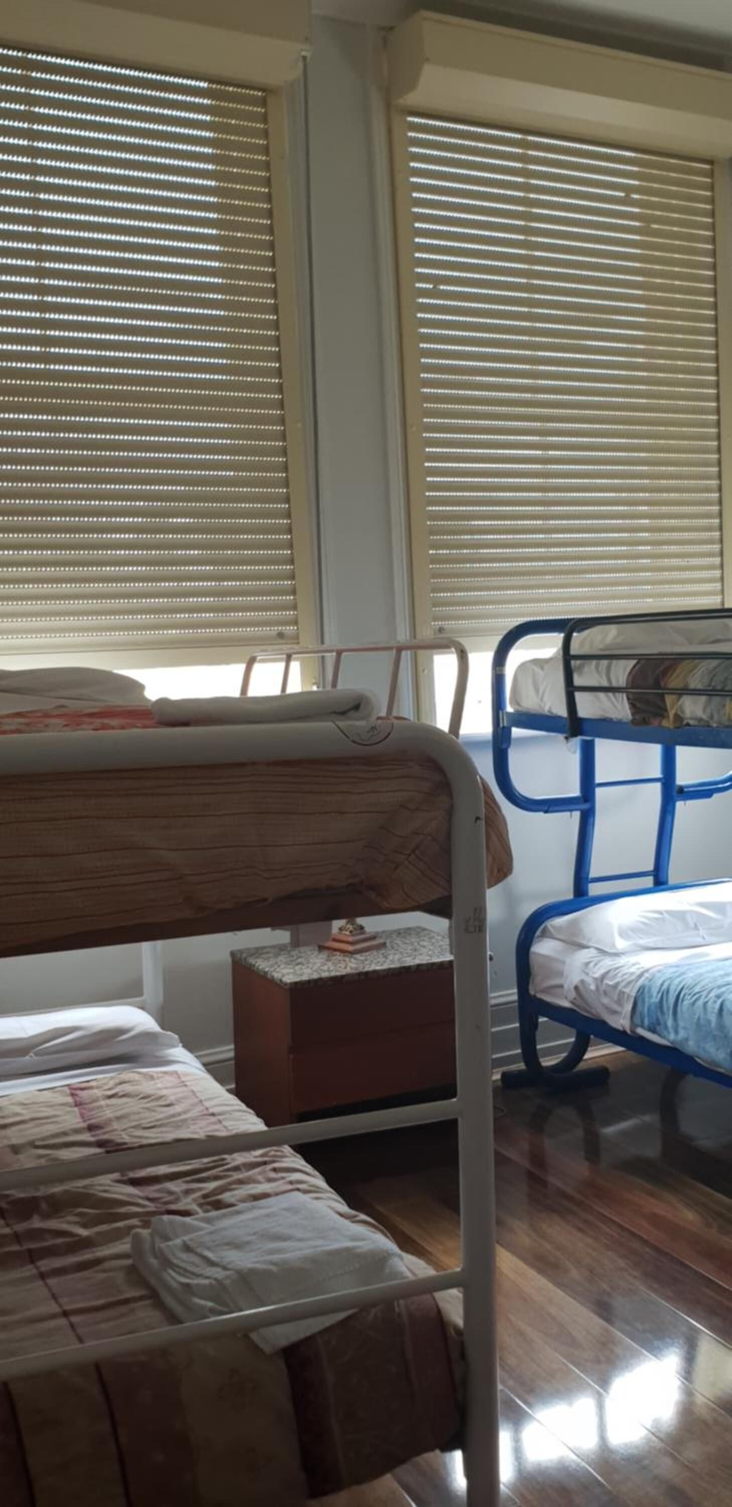 A room with two bunk beds, a wooden headboard, a small wooden cabinet, and a window with blinds.