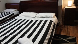 Dos camas individuales con ropa de cama a rayas blancas y negras, un cabecero de madera y una lámpara de noche.
