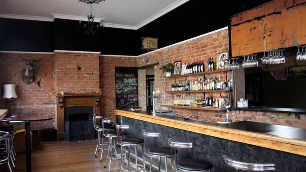 Una zona de bar con pared de ladrillo, mostrador de madera y taburetes.