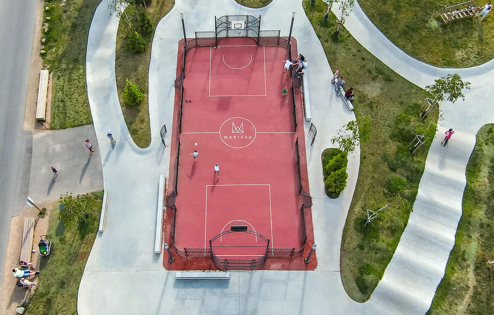 An aerial view of a basketball court with a Marissa logo, surrounded by a curved pathway and greenery.