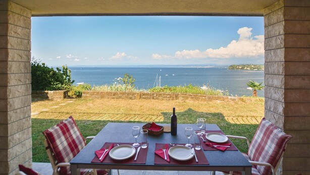 Ein Essbereich im Freien mit Tisch für vier Personen mit Blick auf die Küste, das Meer und das entfernte Land.