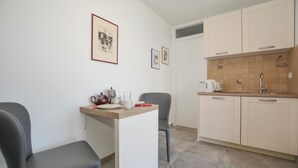 Eine kleine Küchenzeile mit Spüle, Wasserkocher und Kaffeemaschine. Zwei Stühle und ein kleiner Tisch mit Teekanne und Tassen.