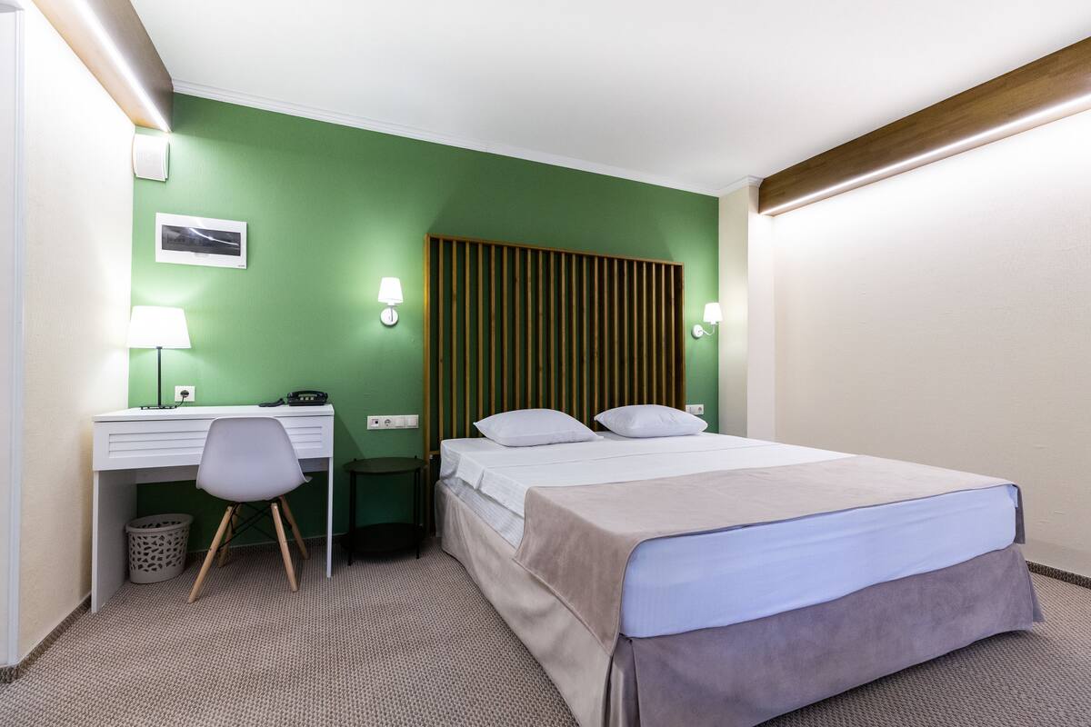A hotel room with a bed, desk, chair, and green walls.