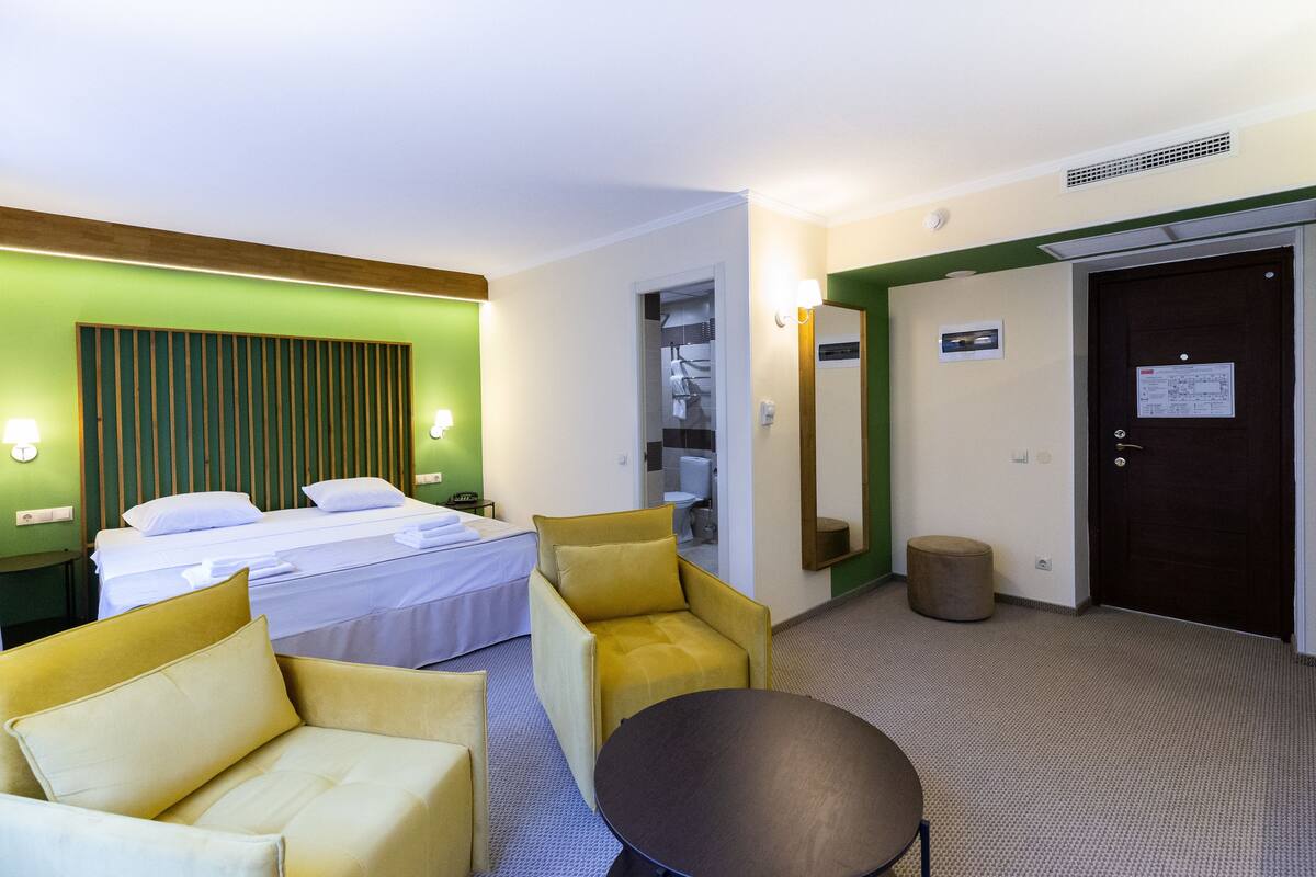 A hotel room with two beds, a sofa, a round table, and a small stool.