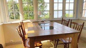 A dining area with a wooden table and chairs, large windows with a view of trees and water, and a lamp on the table.