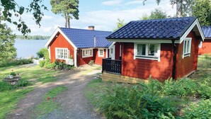 A row of red cabins with blue roofs, a gravel path leading to them, and a lake in the background.