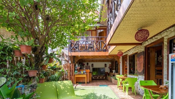 A courtyard with a green sofa, a TV, and a dining area with green chairs. - Balay Paragua Annex (El Nido)