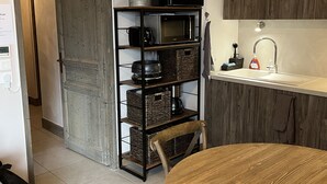 Eine kompakte Küche mit einem runden Holztisch, einer eingebauten Mikrowelle und einem Regal mit Küchenutensilien.