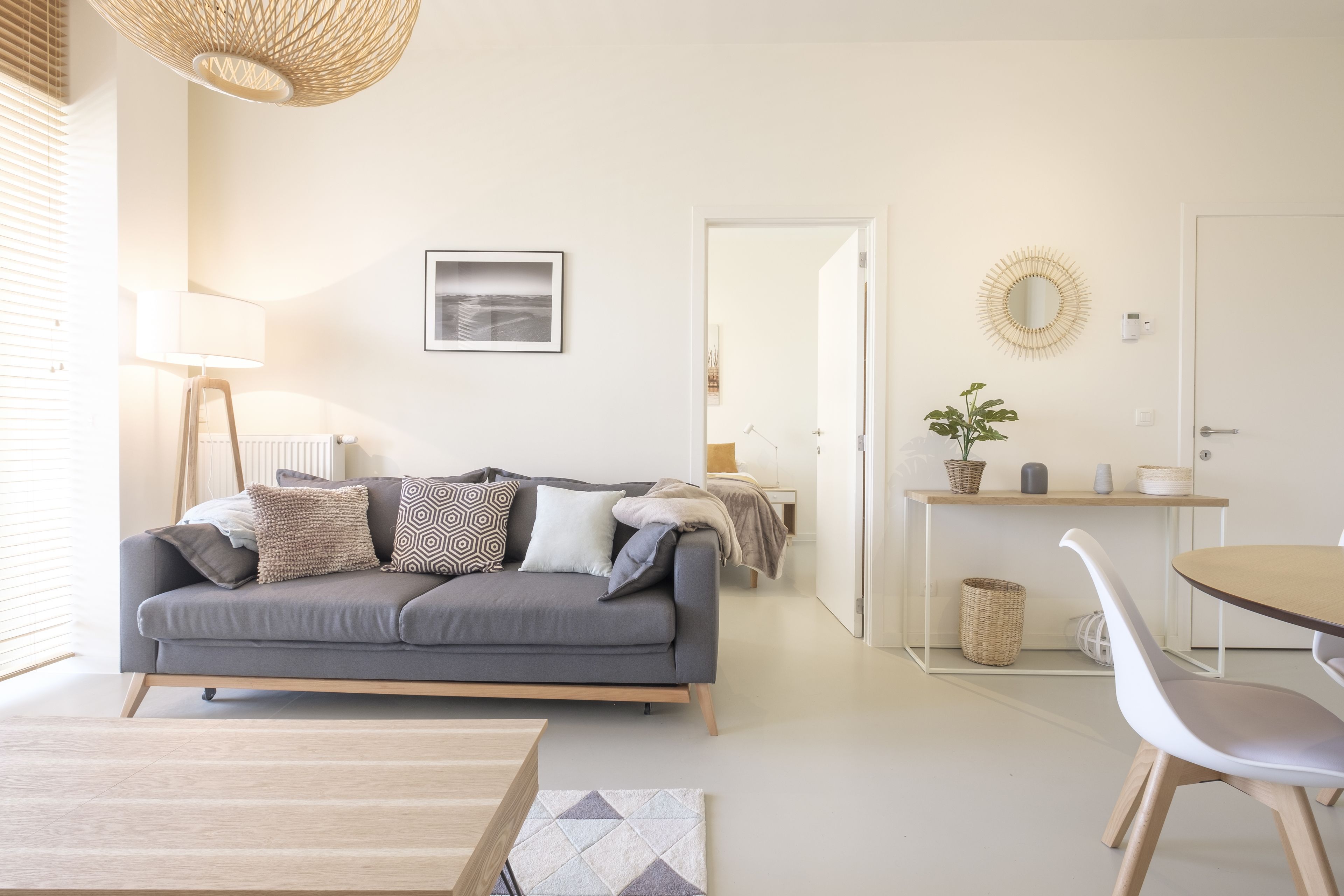A modern living room with a grey sofa, a wooden coffee table, and a dining area with a round table and white chairs.