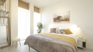 Un dormitorio con cama, mesita de noche, lámpara y ventana con persianas.
