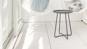 Un balcón luminoso con sillas de mimbre blanco y una pequeña mesa redonda.