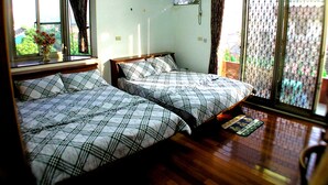 Ein Zimmer mit zwei Betten, einem fensterbelaubten Fenster, einer Klimaanlage und Blick durch ein Insektengitter.