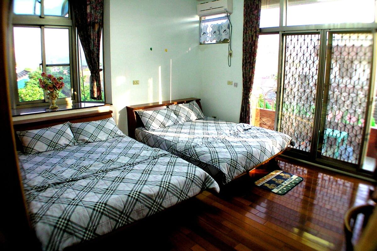Une chambre avec deux lits, une fenêtre avec des rideaux, un appareil de climatisation et une vue à travers un moustiquaire.