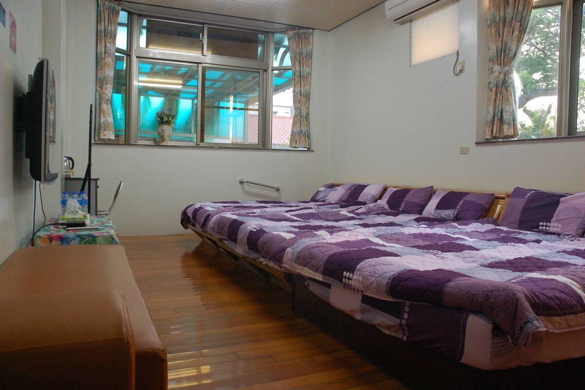 Une chambre à coucher avec un lit, un banc, une télévision et une fenêtre avec des rideaux.
