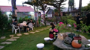 Un espace extérieur aménagé avec des tables et des chaises, entouré de plantes en pot et bordé d’un chemin de pierres.