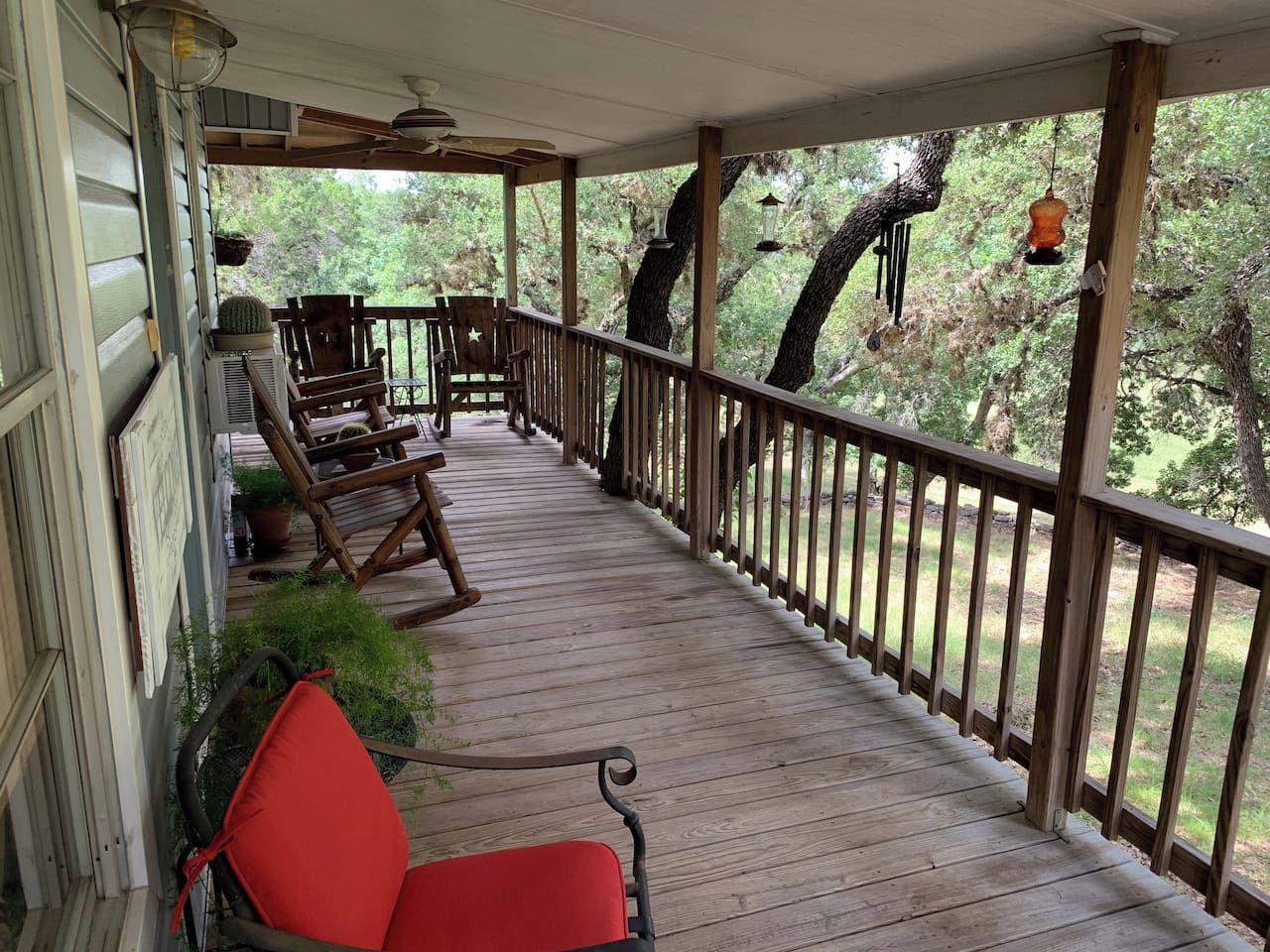 A covered porch with wooden railings, a rocking chair, and a red chair.