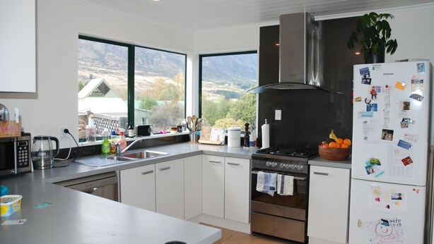 Eine moderne Küche mit weißen Schränken, Edelstahlgeräten und einem großen Fenster mit Blick auf die Berge.