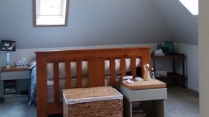 Ein gemütliches Schlafzimmer im Dachgeschoss mit schrägen Wänden, einer Holzbank, einem kleinen Tisch und einem gewebten Korb.