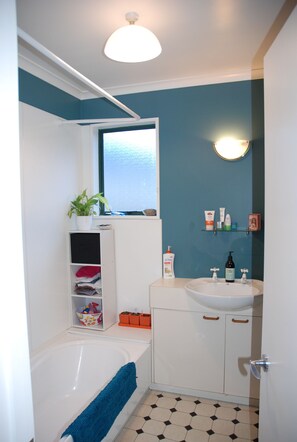 Bathroom features a bathtub, sink, and mirror, with a shelf for toiletries.