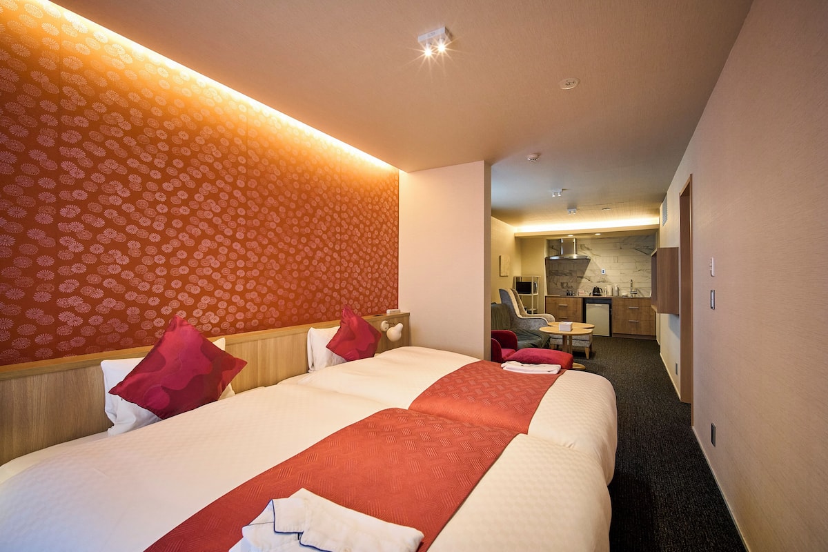 A hotel room with two beds, a kitchenette, and a bathroom.