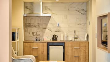 A compact kitchen with marble backsplash, wooden cabinets, and a small refrigerator.
