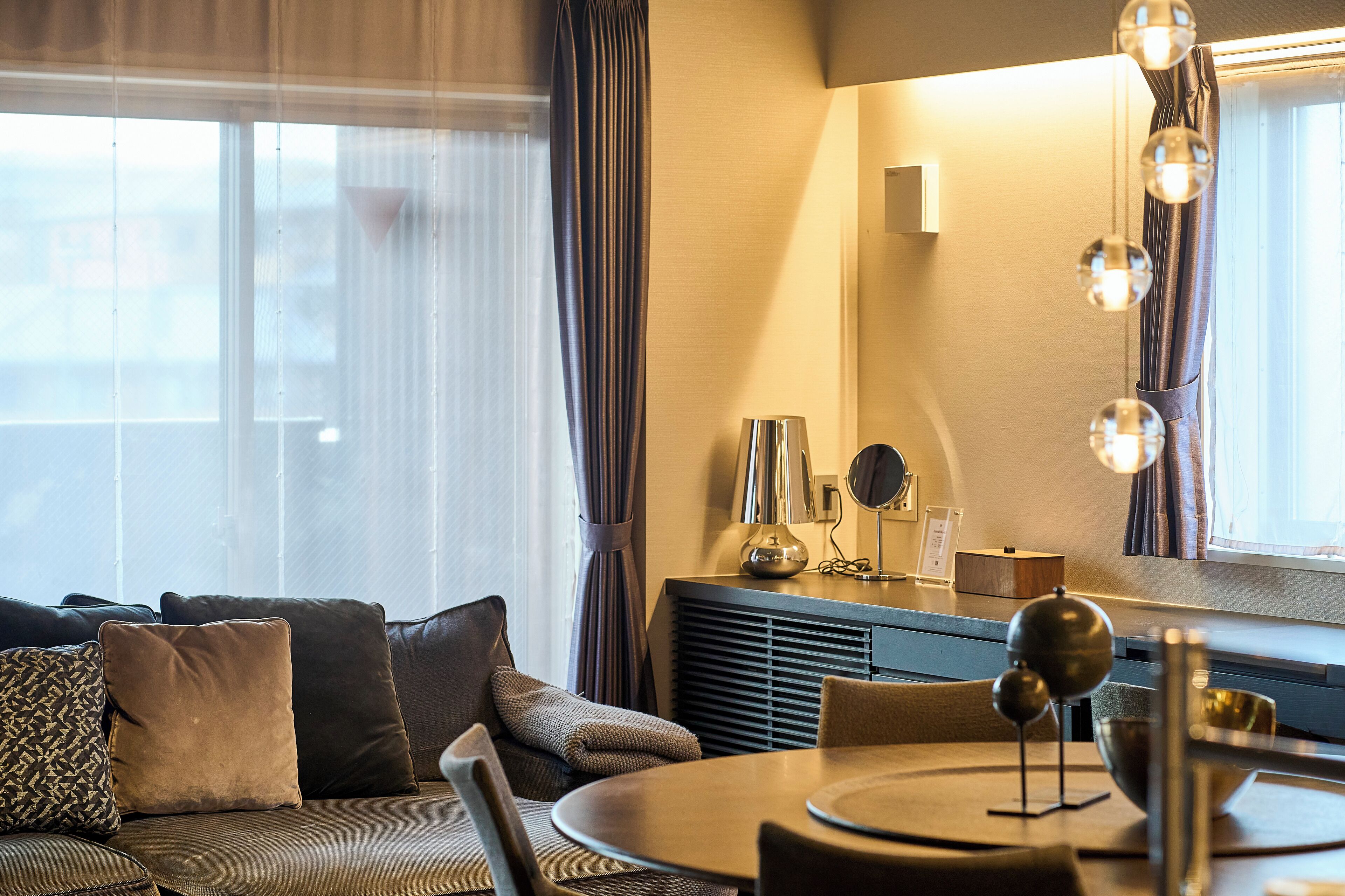 Una habitación de hotel moderna con sofá, mesa de comedor y un ventanal con cortinas.