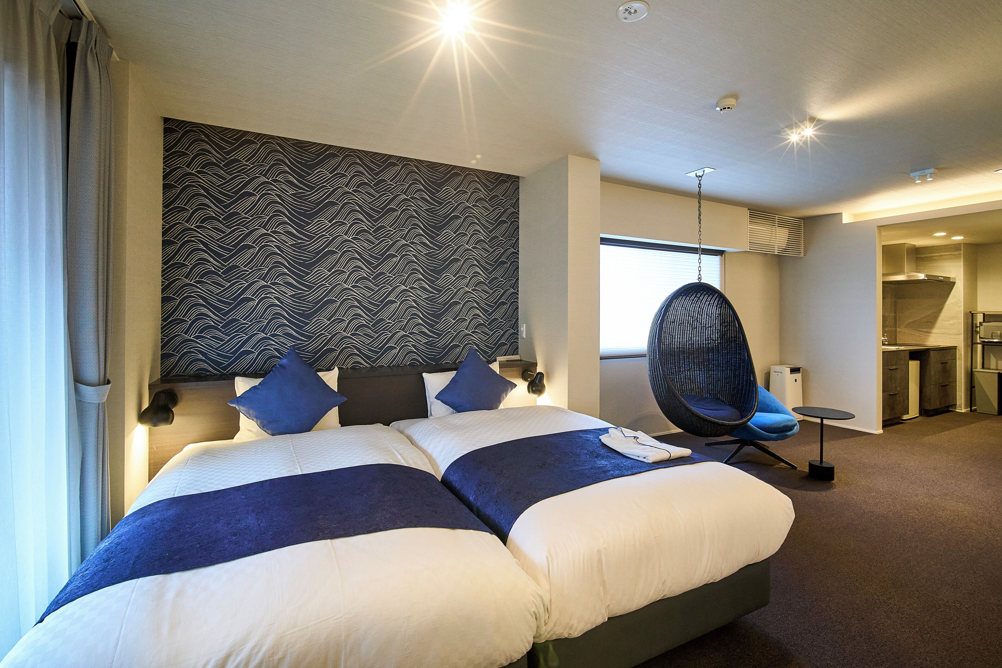 A modern hotel room with a large bed, a hanging chair, and a view of the kitchen area.