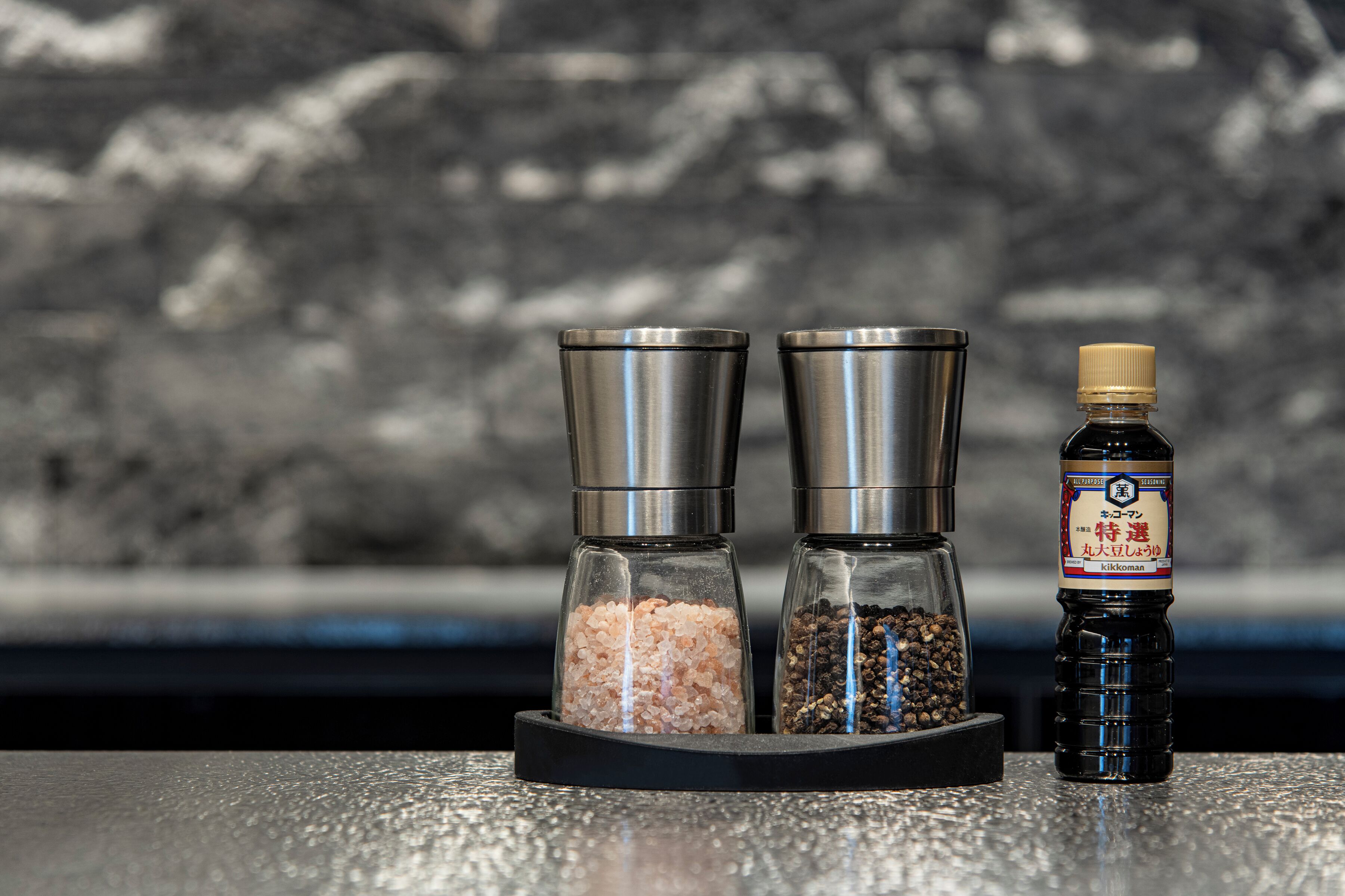 Two salt and pepper shakers and a bottle of soy sauce on a countertop.