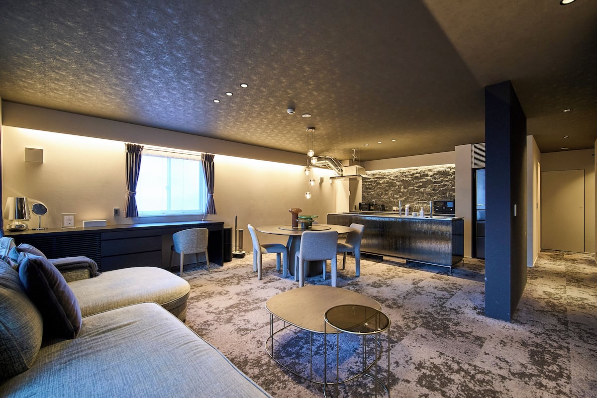 A modern kitchen with a built-in island, a dining area with a round table and chairs, and a living area with a sofa and a coffee table.