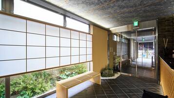 Uma área de recepção com um banco de madeira, janelas amplas e vista para o verde lá fora.